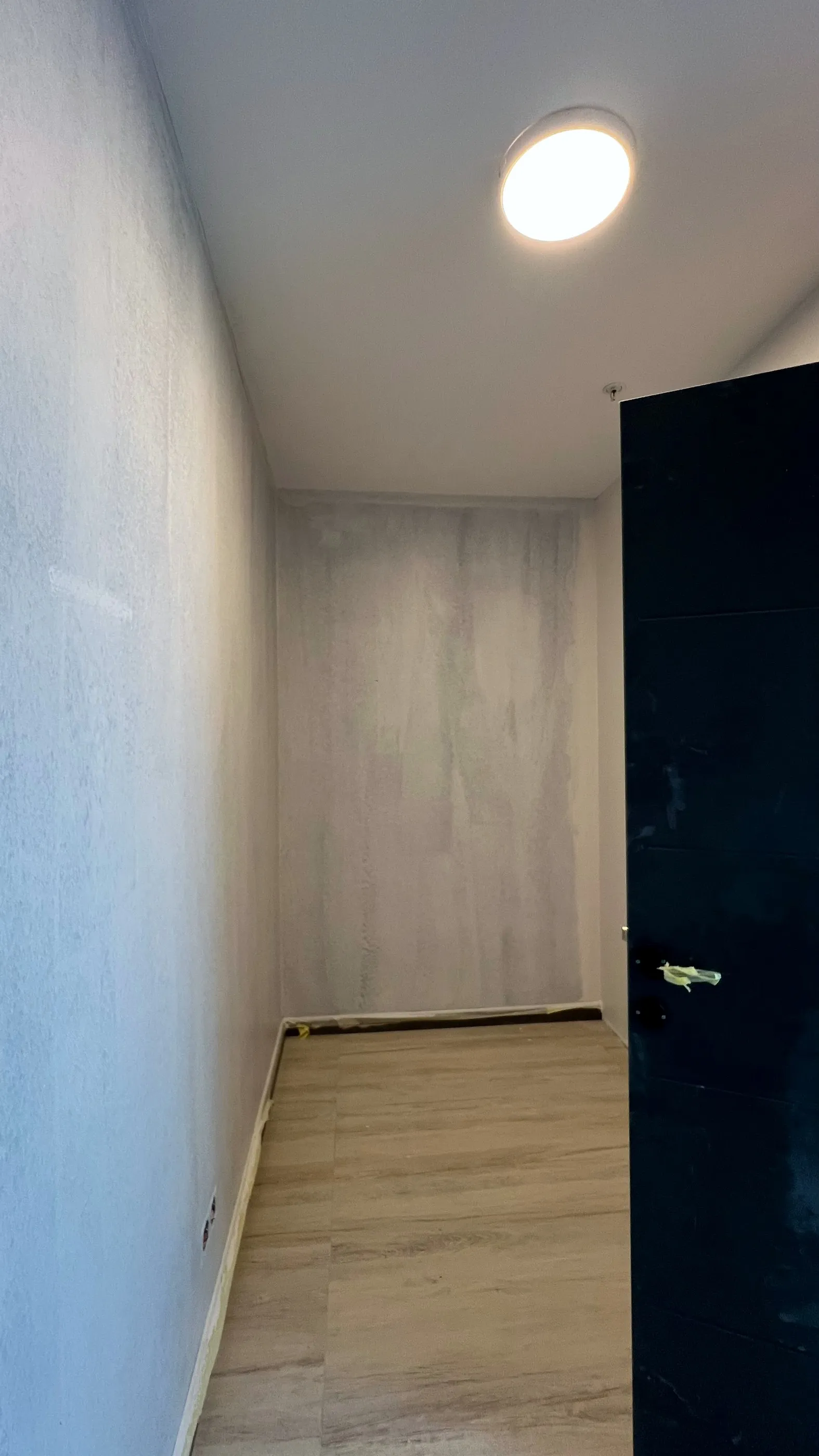 Beton efektli duvarları ve koyu renk kapısıyla tamamlanmış oda