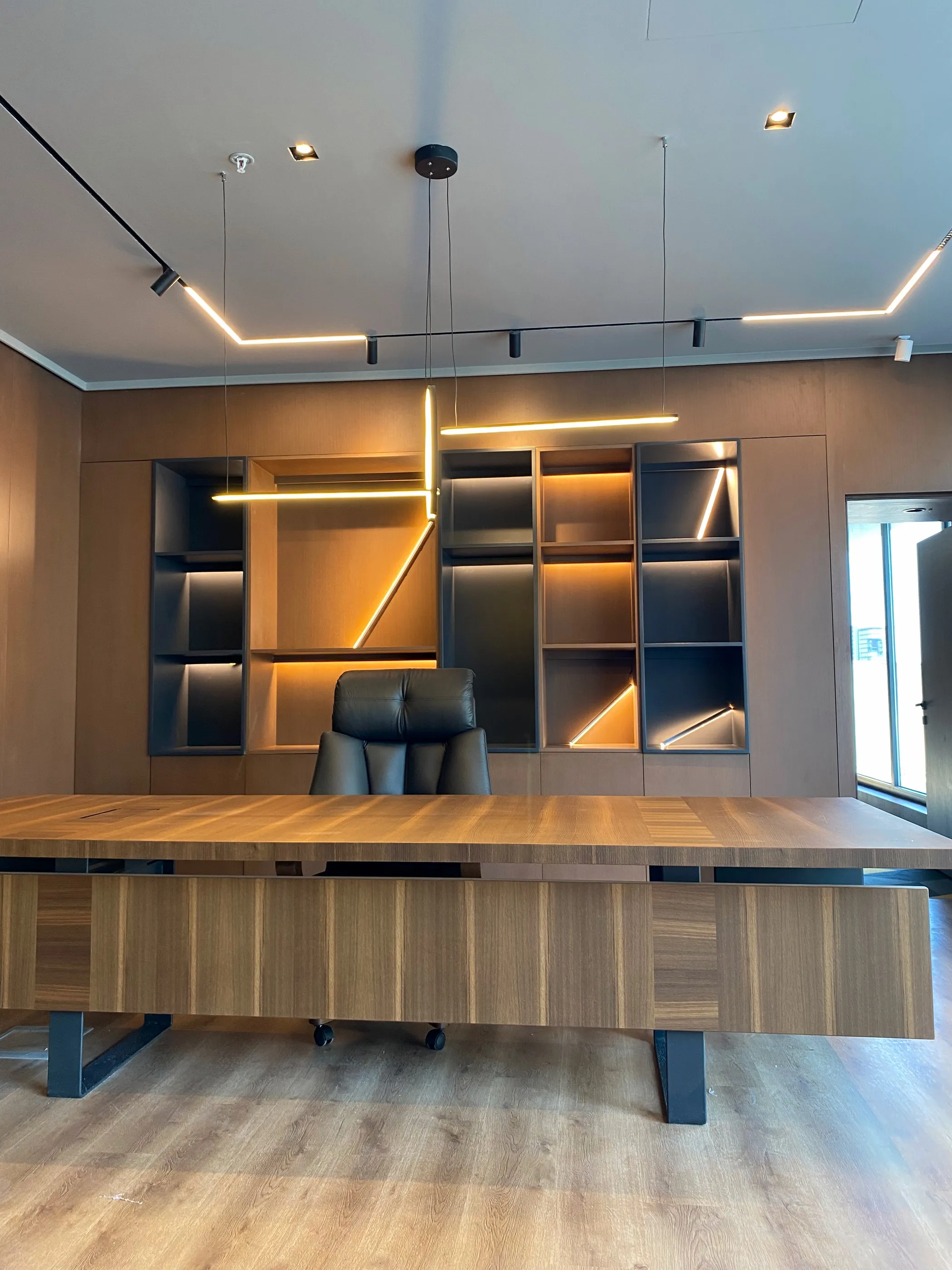 Ahşap çalışma masası ve arkasında gizli LED aydınlatmalı, geometrik bölmeli kitaplık